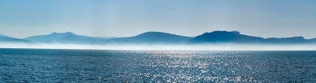 Seascape with low fog clouds over sea water in early morning with sun lights, nature backgroundの写真素材