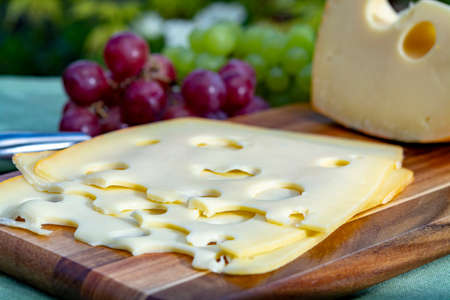 Dutch Maasdam hard cheese with holes, piece and sliced, served with grapes outdoor in green gardenの写真素材