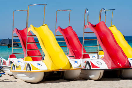 Colorful pedal boats with slides for rent on sandy beach with blue sea water