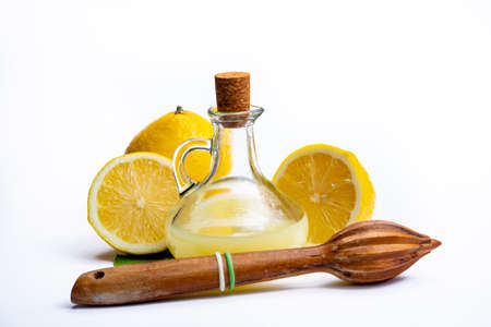 Fresh lemon juice made from ripe yellow Sicilian lemons used for cooking in glass bottle on olive wood plate isolated on white backgroundの写真素材