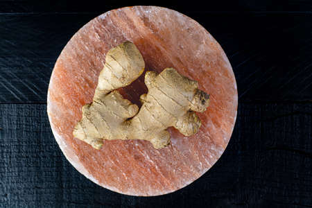 Fresh ginger roots on persian pink salt board close up on black wooden background, asian food conceptの写真素材