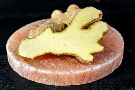Fresh ginger roots on persian pink salt board close up on black wooden background, asian food...