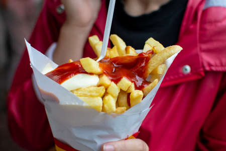 Eating of Belgian fried potatos chips with ketchup and mayonnaise, street fast food, unhealthy food