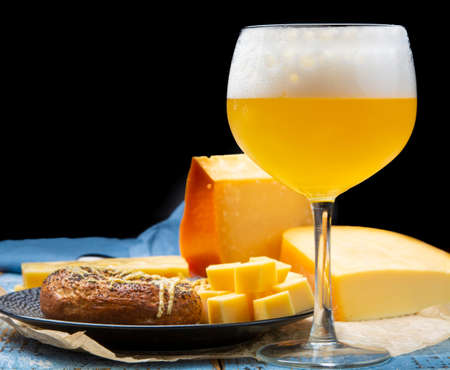 Cold belgian beer in glass served in cafe with variety of hard cheeses, tasty european food close upの写真素材