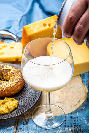 Pouring of cold belgian beer in glass, served in cafe with variety of hard cheeses, tasty european food close upの写真素材