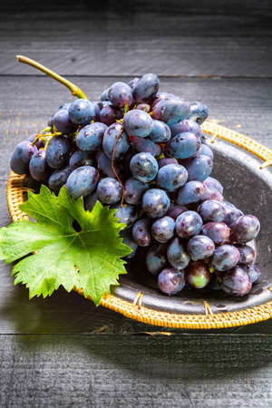 Bunch of ripe blue-black table grapes with leaf served on black plate on black wooden backgroundの写真素材