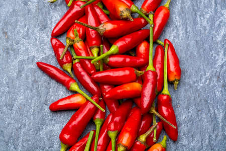 Fresh small red hot chili peppers on grey background close up