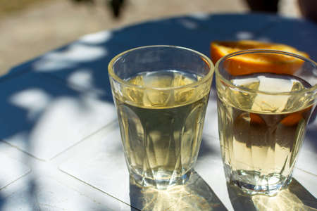 White wine served outside in garden on white table with fresh orange in sun lights close up