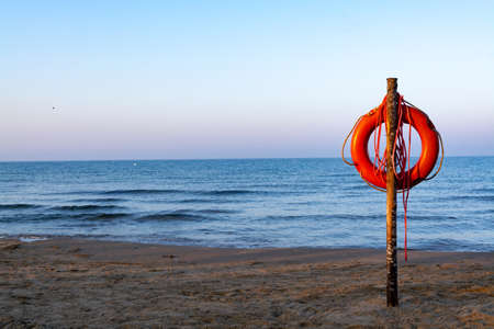 Red lifebuoy with rope on sandy beach, life save in sea water concept copy space