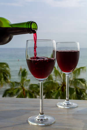 Waiter pouring red wine in glasses in lounge bar with sea view and palm trees close upの写真素材