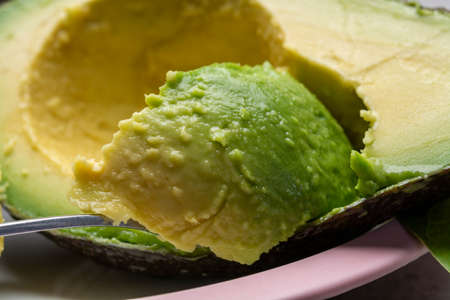 Eating of fresh ripe green organic hass avocado fruit with spoon close up