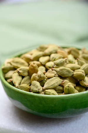 Green pods of cardamom spice in green bowl close up