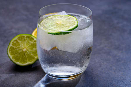 Cold drinking mineral water served in glass with ice cubes and green lime close up