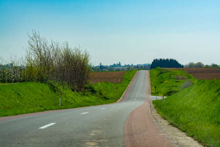 Asphalt road and spring landscape with farmers plowed fields and green grass, nature backgroundの写真素材
