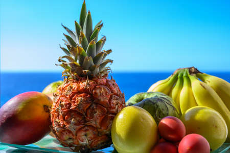 Tropical fruits collection, custard apple or green ripe cherymoia, passion fruit, pineapple, mango, tamarillo, banana exotic fruits on blue sea background in sunny dayの写真素材