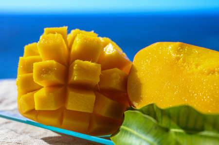 Fresh ripe sweet yellow mango fruit served on glass plate with blue seaview background, close upの写真素材