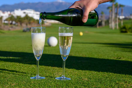 Pouring of bubbles white champagne or cava wine during golf competition event or celebration on green golf club grass with mountains view in sunny dayの写真素材