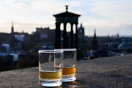 Scotch single malts or blended whisky spirits in glasses with Calton hill in Edinburgh on...