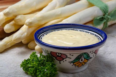 Bunch of fresh uncooked white asparagus and hollandaise sauce in bowl, tasty vegetarian foodの写真素材