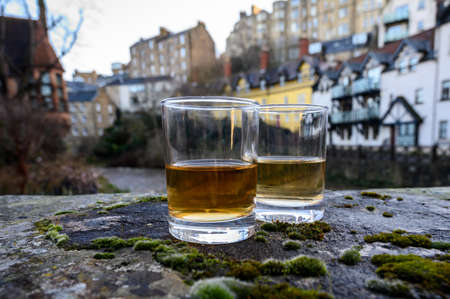 Scotch single malts or blended whisky spirits in glasses with old houses of Edinburgh city on background, Scotland, UKの写真素材