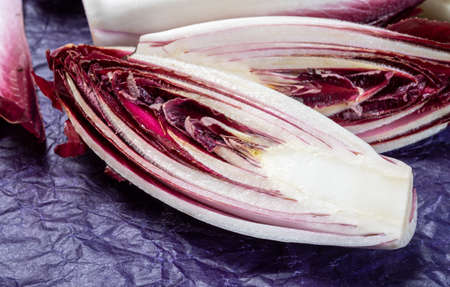 Fresh organic Belgian endivi or green and red chicory lettuce close up in violet protective paper