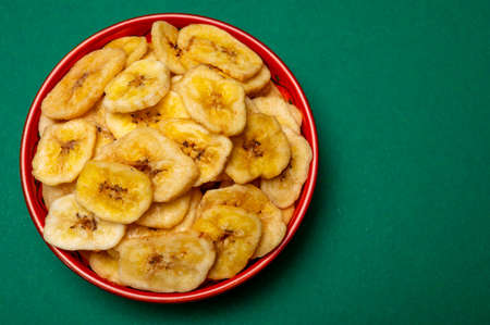 Healthy sweet snack, crispy dehydrated unsugared banana chips in bowl on green backgroundの写真素材