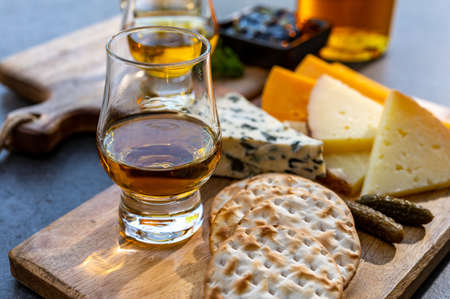 Whiskey and cheese pairing, tasting whisky glasses and plate with sliced cheeses close up
