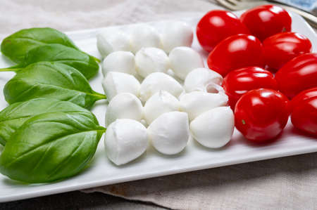 Italian food served as flag of Italy Tricolore with fresh fresh green basil, white mini mozzarella cheese and red cherry tomatoes close upの写真素材