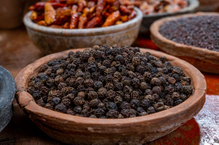 Indian spices collection, dried black peppercorns  and another spices in clay bowls close up