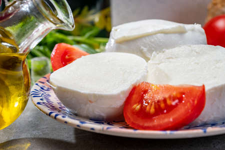 Making of fresh caprese salad with soft Italian cheese from Campania buffalo mozzarella with ripe tomatoes, basil and olive oil close upの写真素材