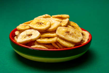 Healthy sweet snack, crispy dehydrated unsugared banana chips in bowl on green backgroundの写真素材
