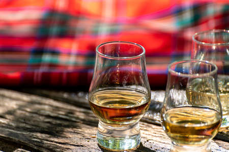 Tasting of different Scotch whiskies on outdoor terrace, dram of whiskey and red tartan close up