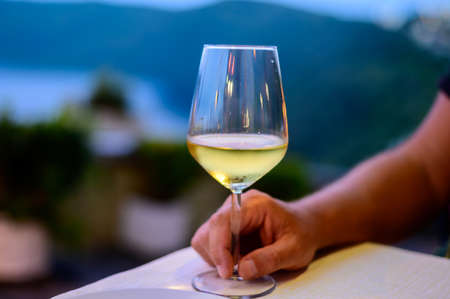 Hand with glass of cold dry white wine served outdoor in cafe at night in Italy close upの写真素材