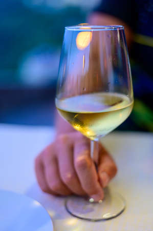 Hand with glass of cold dry white wine served outdoor in cafe at night in Italy close upの写真素材