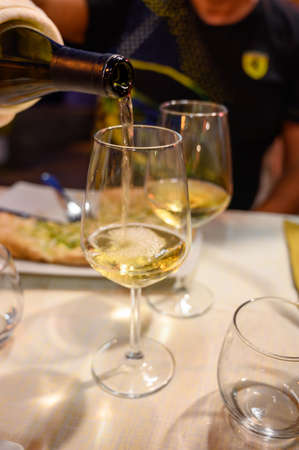 Pouring in glass cold dry white wine in outdoor cafe at night in Italy close upの写真素材