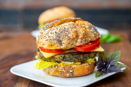 Eating of fresh and healthy vegetarian burgers with grilled spinach or pumpkin burgers, organic buns and vegetables close upの写真素材