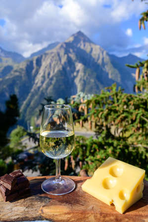 Glass of swiss or savoy dry white wine and yellow emmental cheese with Alpine mountains peaks on background in sunny dayの写真素材