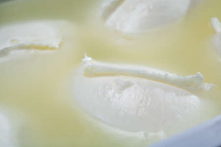 Cheese shop, fresh handmade soft Italian cheese from Campania, white balls of buffalo mozzarella cheese made from cow milk in container with water close upの写真素材
