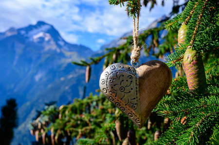 Green Christmas tree with cones growing in French Alps mountains decorated with hanging wooden heart and mountain peaks on backgroundの写真素材