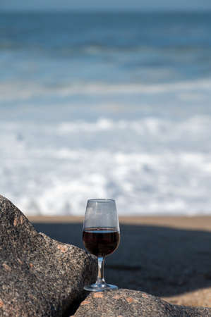Tasting of different fortified dessert ruby, tawny port wines in glass on sandy beach with view on waves of Atlantic ocean near Vila Nova de Gaia and city of Porto, Portugalの写真素材