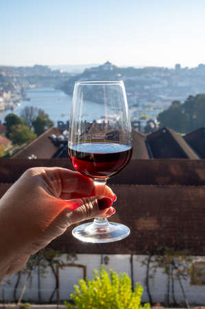 Tasting of different fortified dessert ruby, tawny port wines in glasses with view on Douro river, porto lodges of Vila Nova de Gaia and city of Porto, Portugal, close upの写真素材