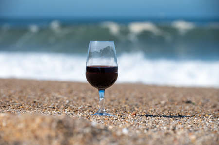 Tasting of different fortified dessert ruby, tawny port wines in glass on sandy beach with view on waves of Atlantic ocean near Vila Nova de Gaia and city of Porto, Portugalの写真素材