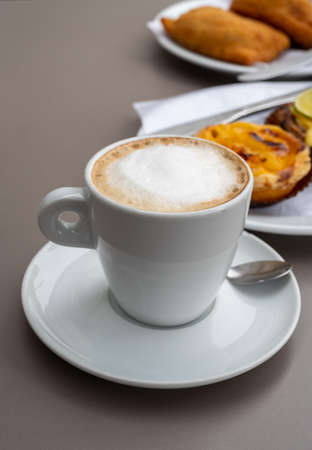 Cup of cappuccino coffee served with traditional dessert pastry in Portugal, nata eggs cream cakes with fruits for breakfastの写真素材