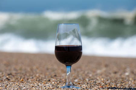Tasting of different fortified dessert ruby, tawny port wines in glass on sandy beach with view on waves of Atlantic ocean near Vila Nova de Gaia and city of Porto, Portugalの写真素材