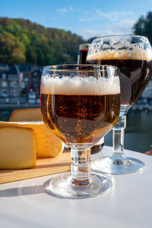 Drinking of dark and strong Belgian abbey beer with cheeses in sunny day with nice view on Maas river and town Dinant, Belgiumの素材 [FY310159724937]