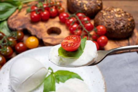 Cheese collection, eating of white soft Italian cheese mozzarella, served with red cherry tomatoes,...
