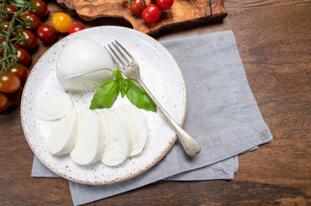 Cheese collection, eating of white soft Italian cheese mozzarella, served with red cherry tomatoes, fresh basil leaves close upの写真素材
