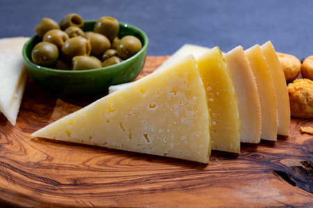 Spanish snacks tapas, variety of sliced goat, sheep, manchego cheeses, green olives, served in...