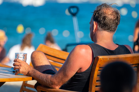 Unidentified man sitting in beach cafe with glass of drink en looking to blue water of Gulf of Saint-Tropez, French Riviera, France in summerのeditorial素材