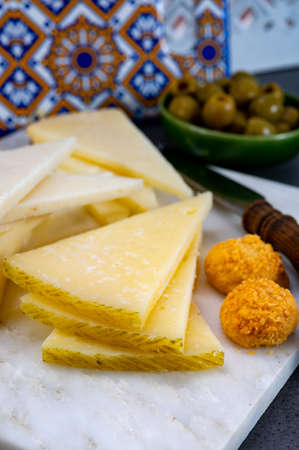 Spanish snacks tapas, variety of sliced goat, sheep, manchego cheeses, green olives, served in...